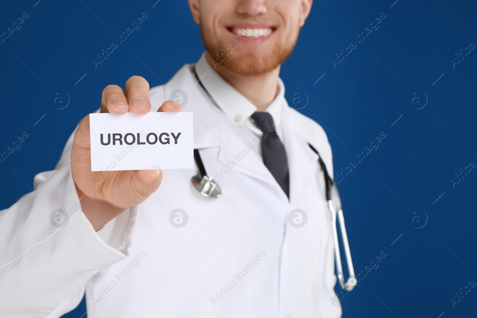 Photo of Male doctor holding card with word UROLOGY on blue background, closeup