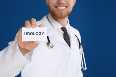 Male doctor holding card with word UROLOGY on blue background, closeup