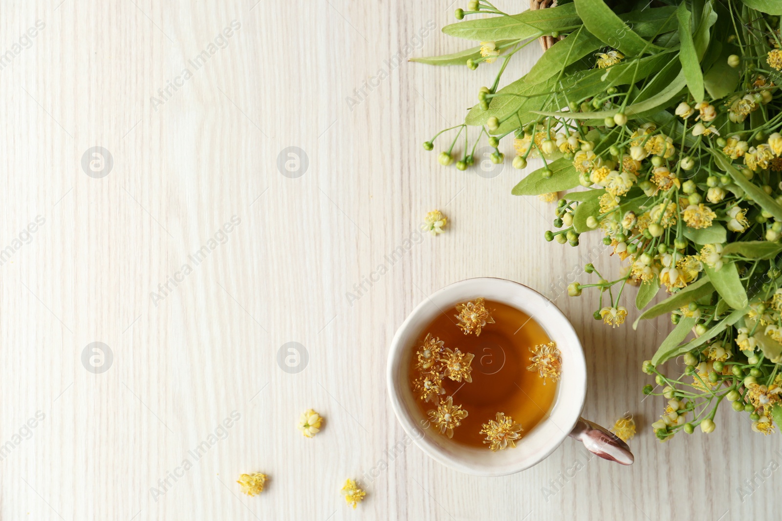 Photo of Cup of aromatic tea with linden blossoms on white wooden table, flat lay. Space for text