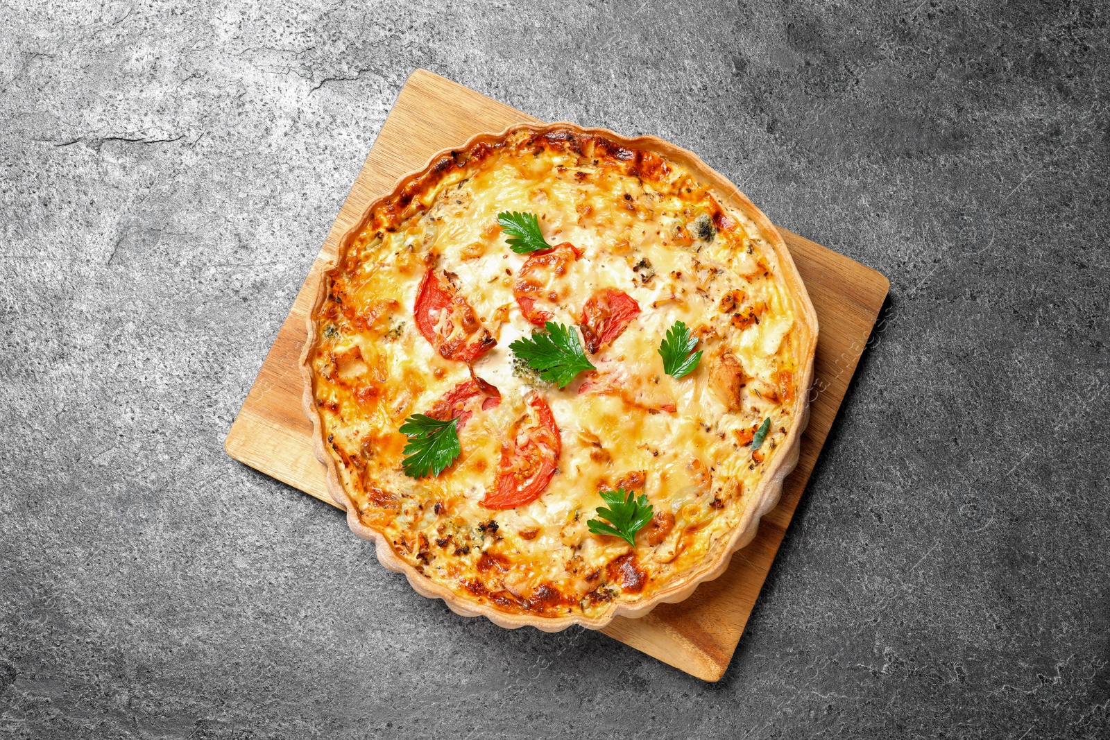 Photo of Tasty quiche with tomatoes, parsley and cheese on grey textured table, top view