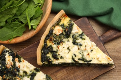 Pieces of delicious homemade quiche and fresh spinach leaves on wooden table, closeup