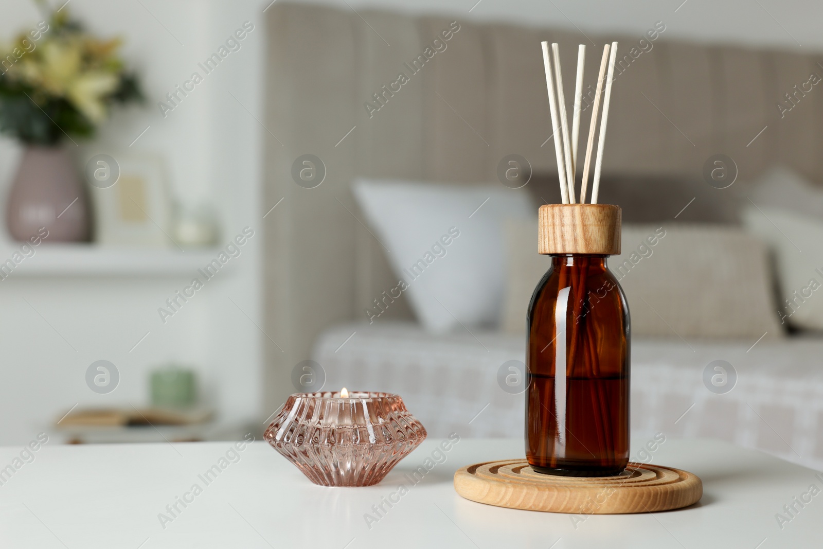 Photo of Aromatic reed air freshener and candle on white table in bedroom. Space for text