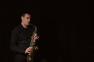 Young man playing saxophone on dark background. Space for text