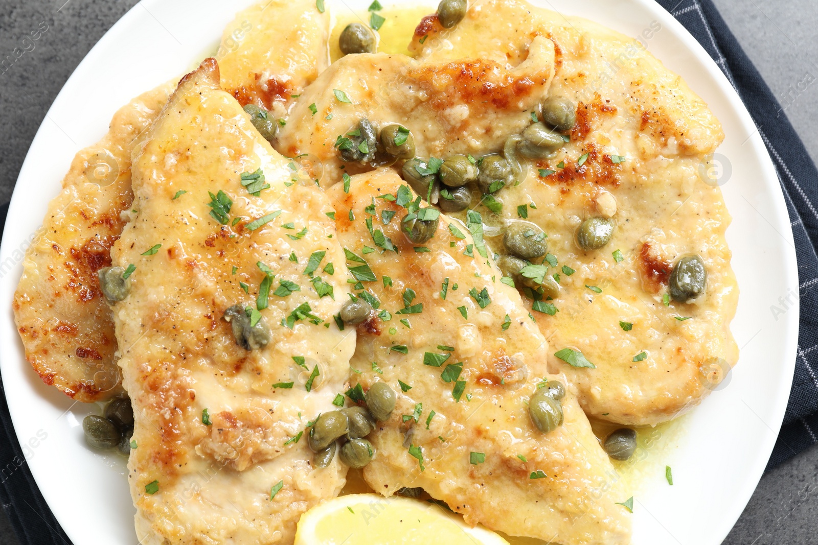 Photo of Delicious chicken piccata with herbs on grey table, top view