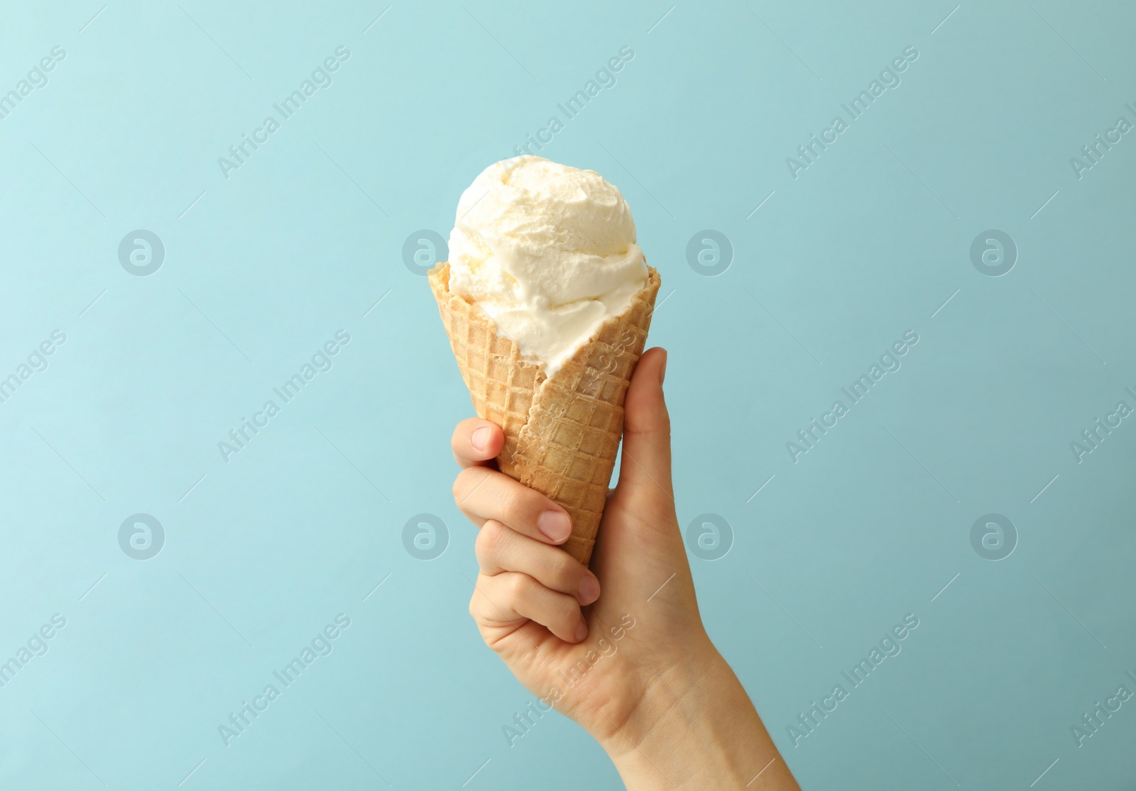 Photo of Woman holding waffle cone with delicious ice cream on light blue background, closeup