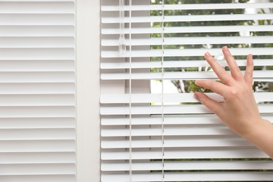 Woman separating slats of window blinds, closeup