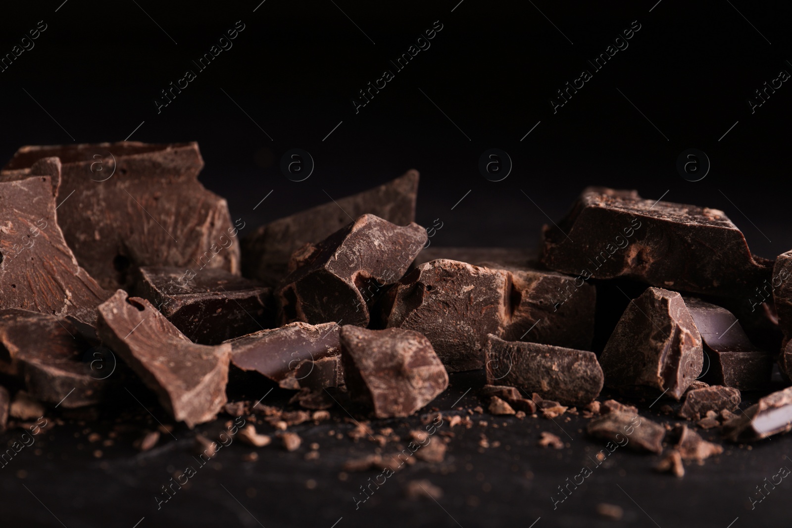 Photo of Pieces of dark chocolate on black table, closeup