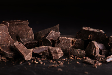 Pieces of dark chocolate on black table, closeup