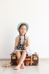 Photo of Adorable little child playing traveler with suitcase indoors