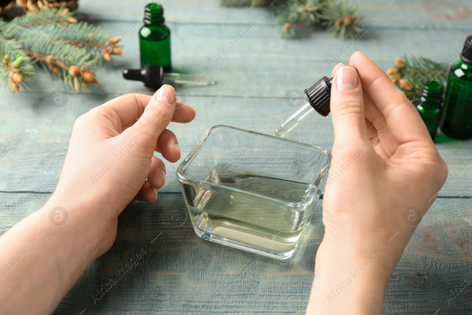 Photo of Woman dripping essential oil into bowl with pipette at wooden table, closeup
