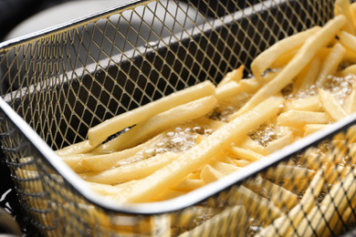 Photo of Cooking delicious french fries in hot oil, closeup