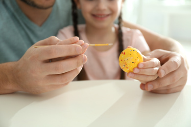 Photo of Father and daughter painting Easter egg at table, closeup