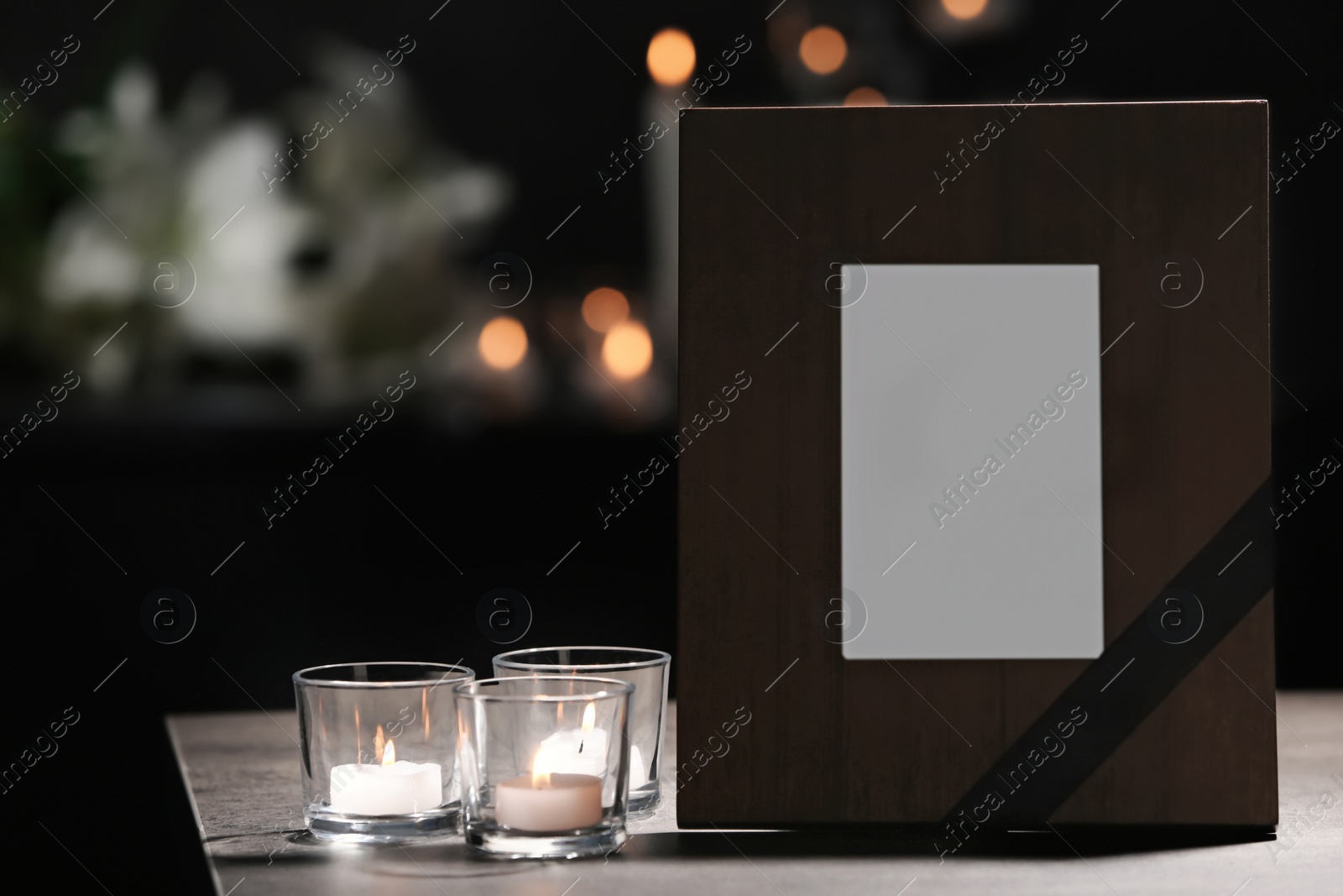 Photo of Funeral photo frame with black ribbon and burning candles on table in dark room