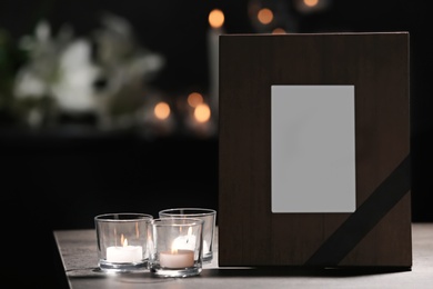 Photo of Funeral photo frame with black ribbon and burning candles on table in dark room