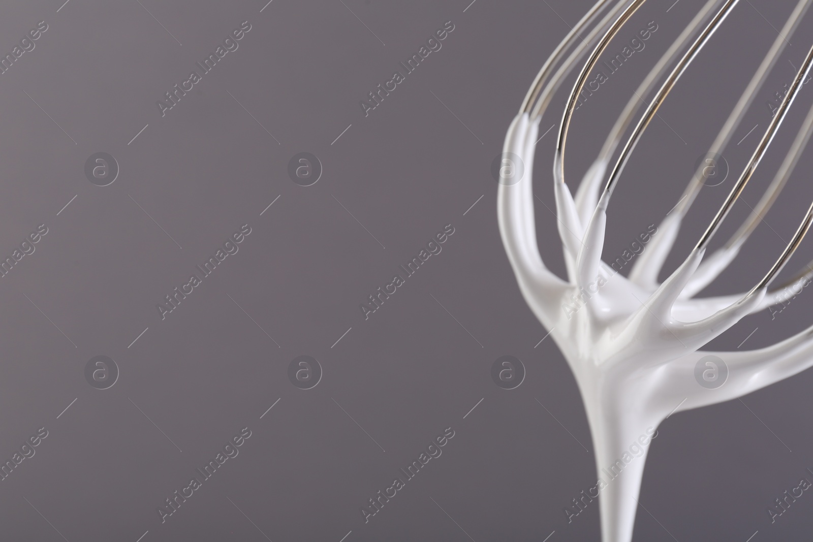 Photo of Whisk with whipped cream on grey background, closeup. Space for text