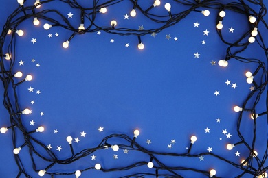 Photo of Glowing Christmas lights on color background, top view