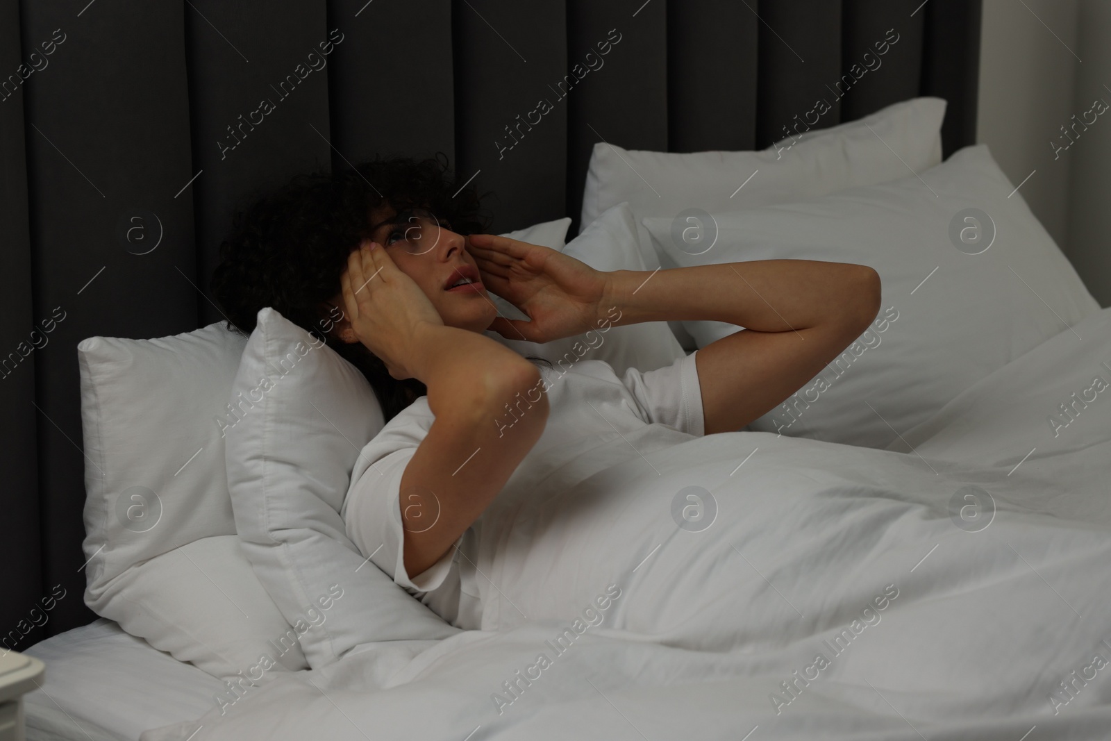 Photo of Young woman suffering from headache in bed at night