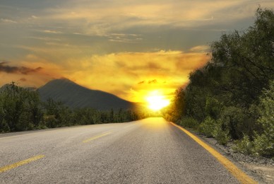 Empty asphalt road, trees and mountains at beautiful sunset