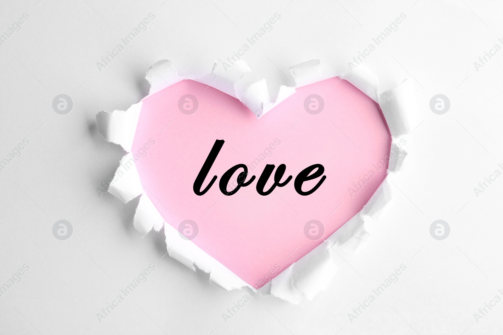 Image of Top view of word Love on pink background, view through torn heart shaped hole in white paper