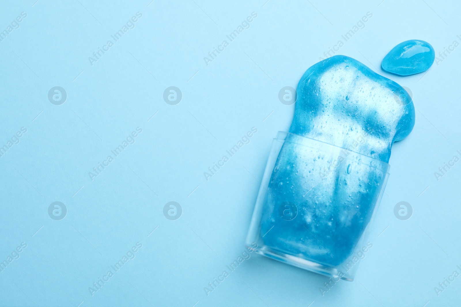 Photo of Overturned plastic container with bright slime on light blue background, top view. Space for text