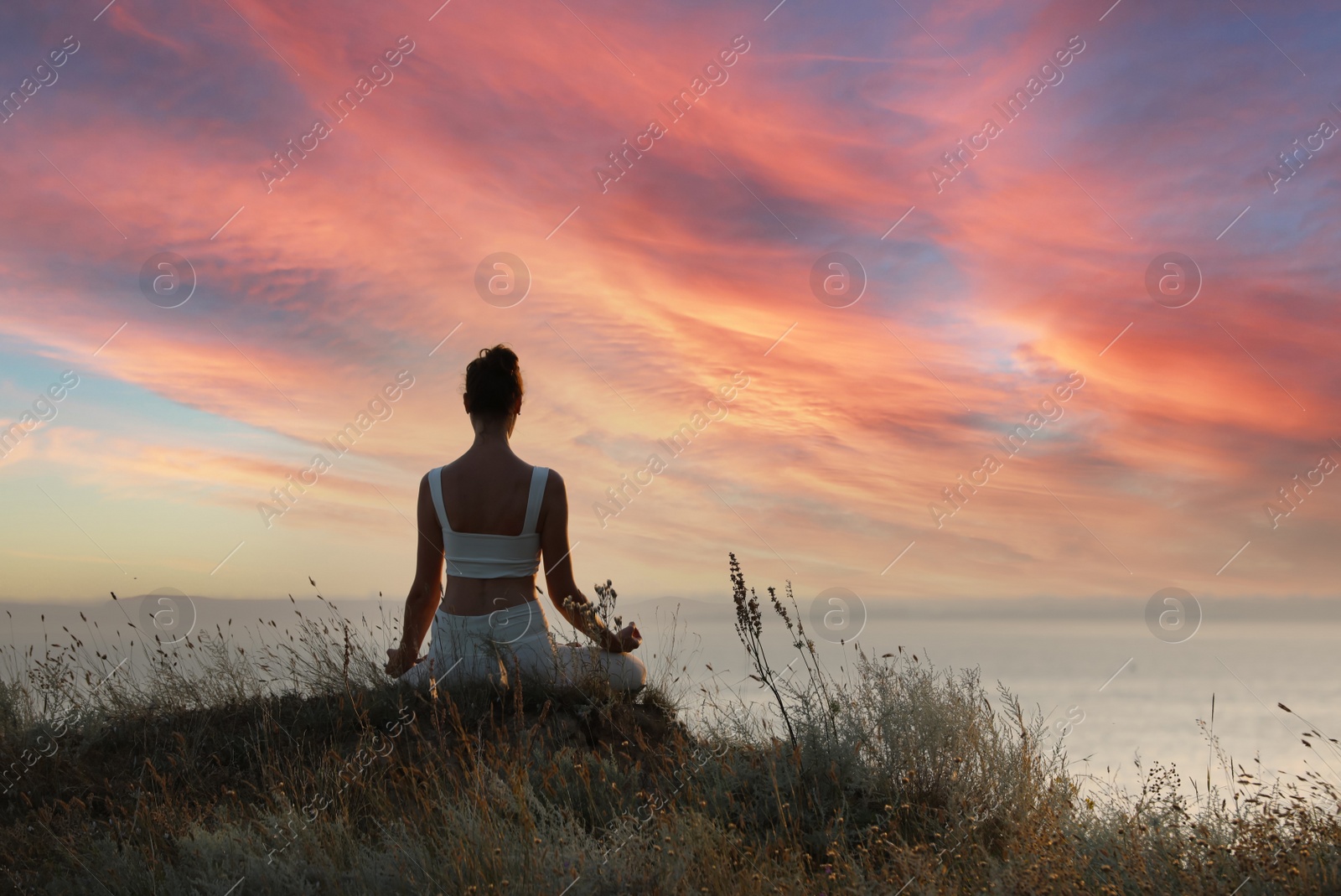 Photo of Woman meditating on hill near sea, back view. Space for text