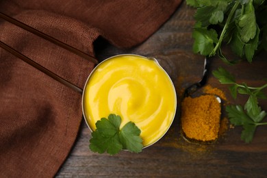 Saucepan with tasty curry sauce, powder and parsley on wooden table, flat lay