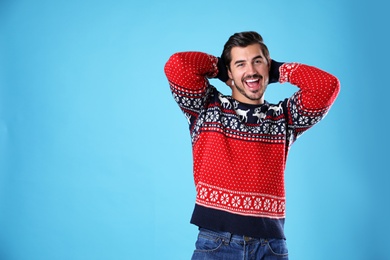 Portrait of happy young man in Christmas sweater on light blue background. Space for text