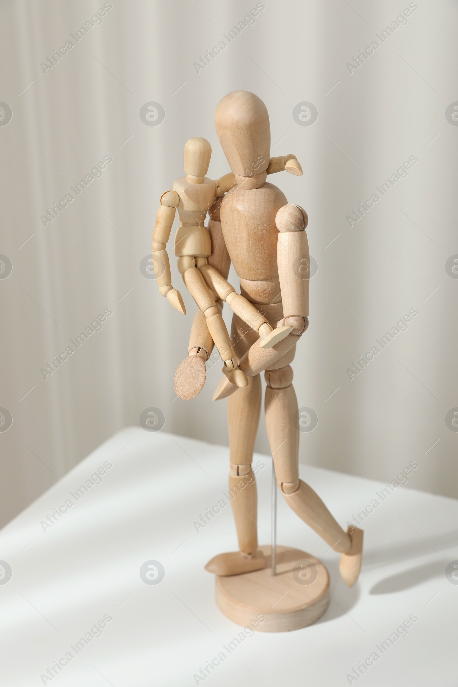 Photo of Wooden mannequins of parent with child on white table against light background. Family Day