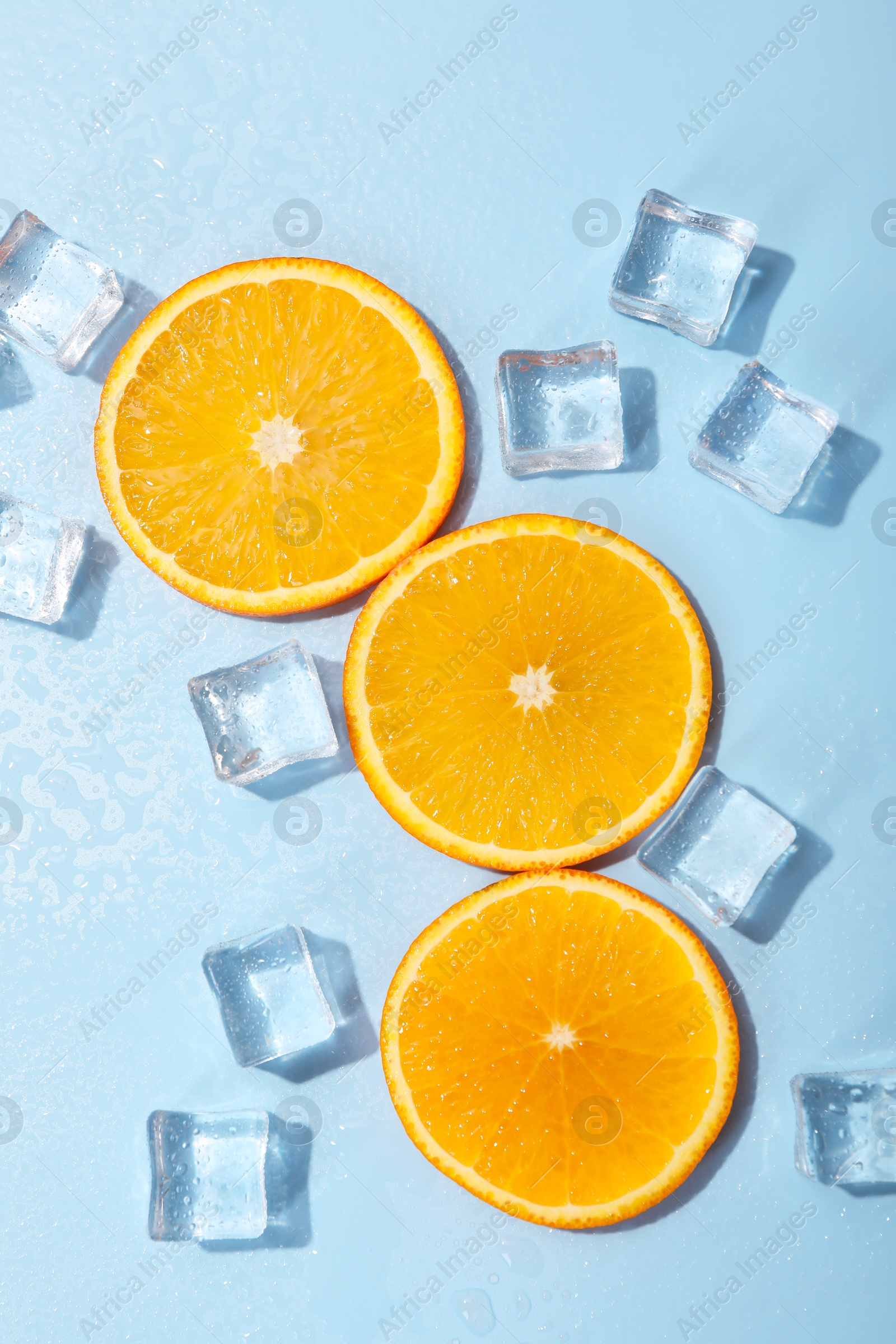 Photo of Slices of juicy orange and ice cubes on light blue background, flat lay