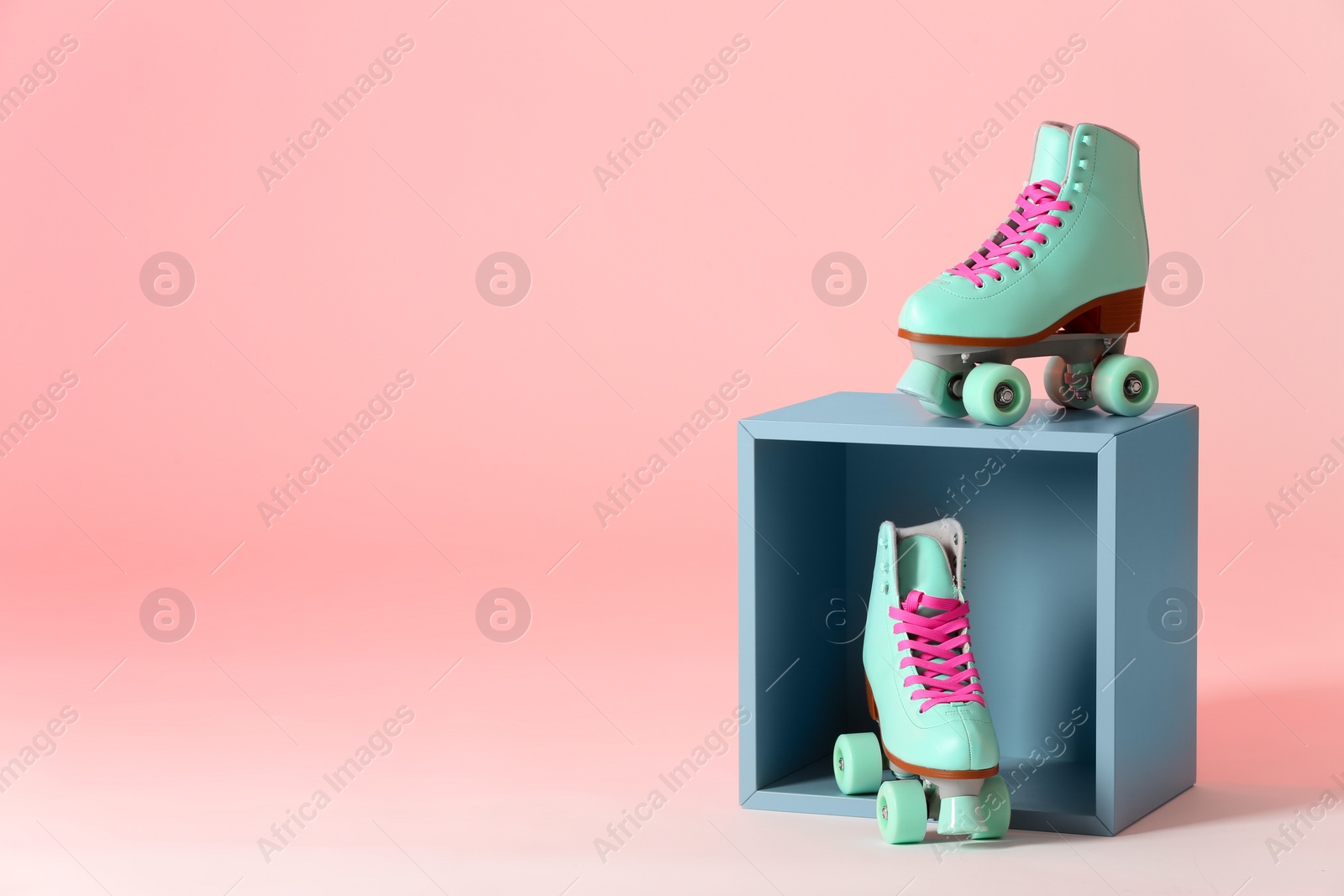 Photo of Pair of vintage roller skates and storage cube on color background. Space for text