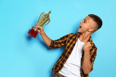 Photo of Happy boy with golden winning cup on blue background