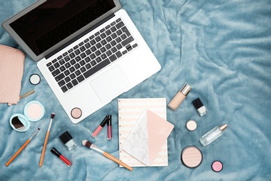 Flat lay composition with laptop, notebook and makeup products for woman on fabric