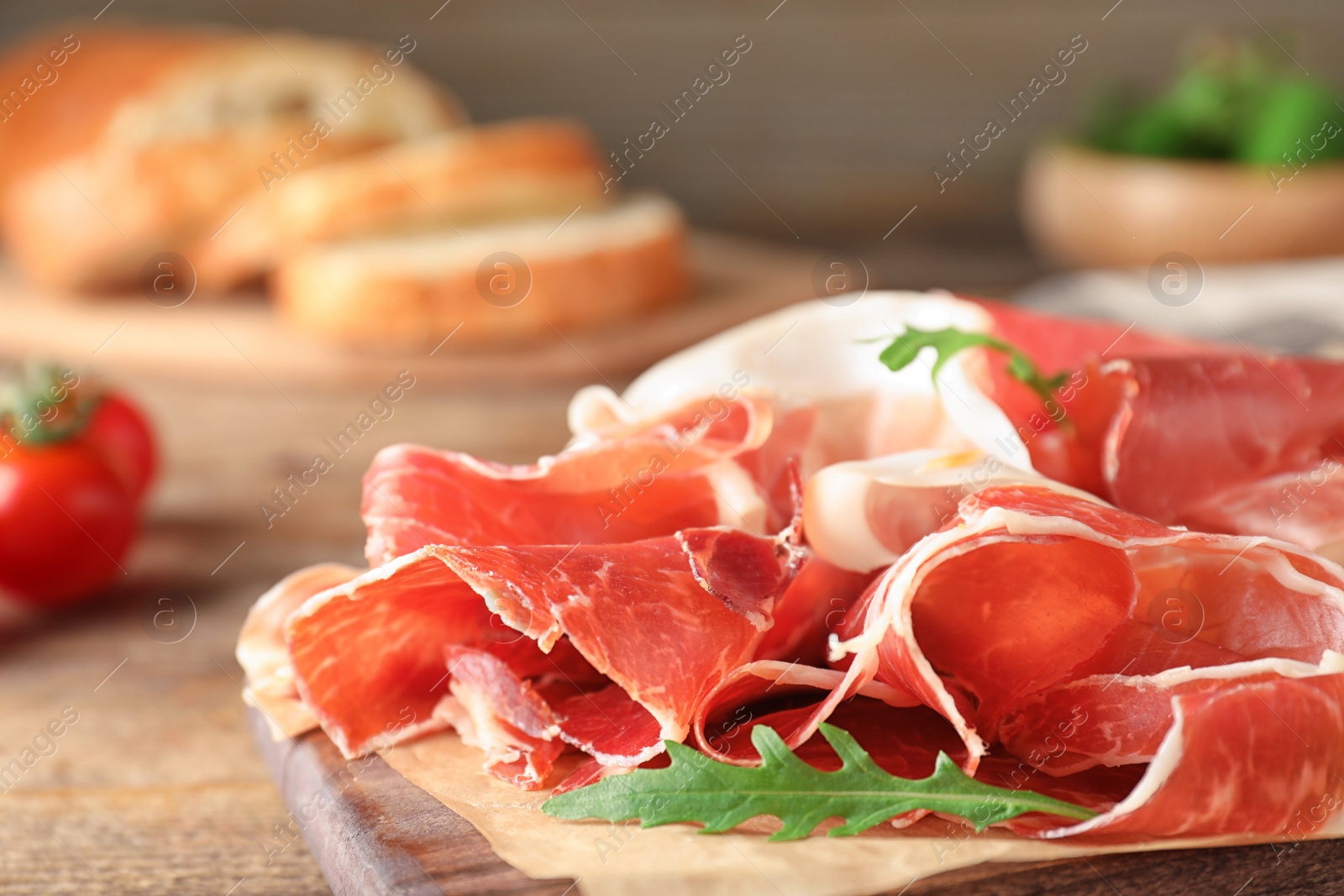 Photo of Pile of tasty prosciutto on wooden table, closeup