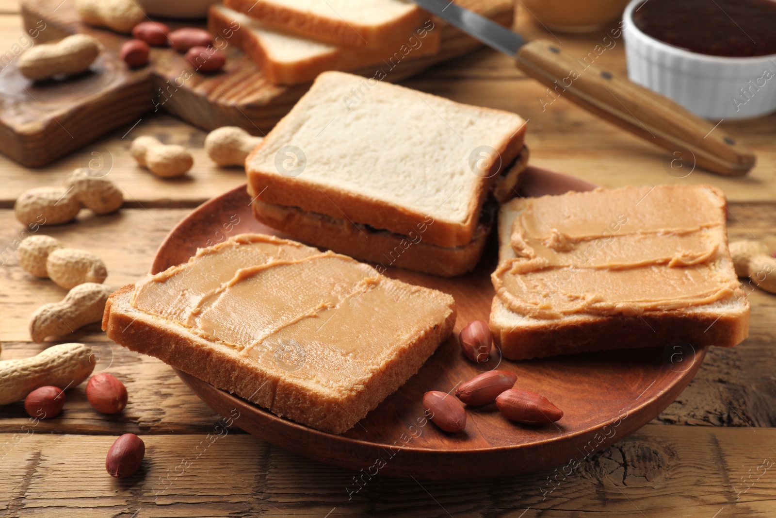 Photo of Tasty peanut butter sandwiches and peanuts on wooden table, closeup