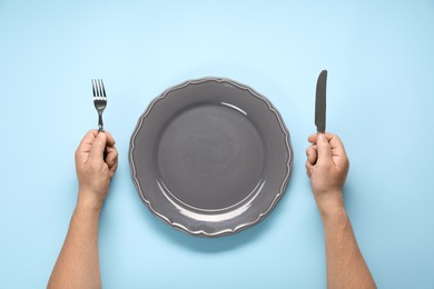 Photo of Man with cutlery and empty plate at light blue table, top view