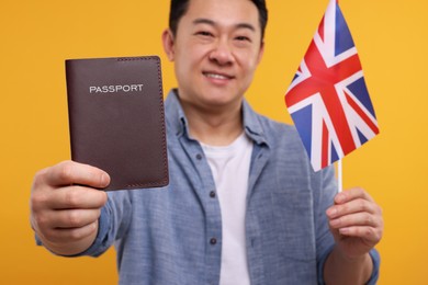 Photo of Immigration. Happy man with passport and flag of United Kingdom on orange background, selective focus