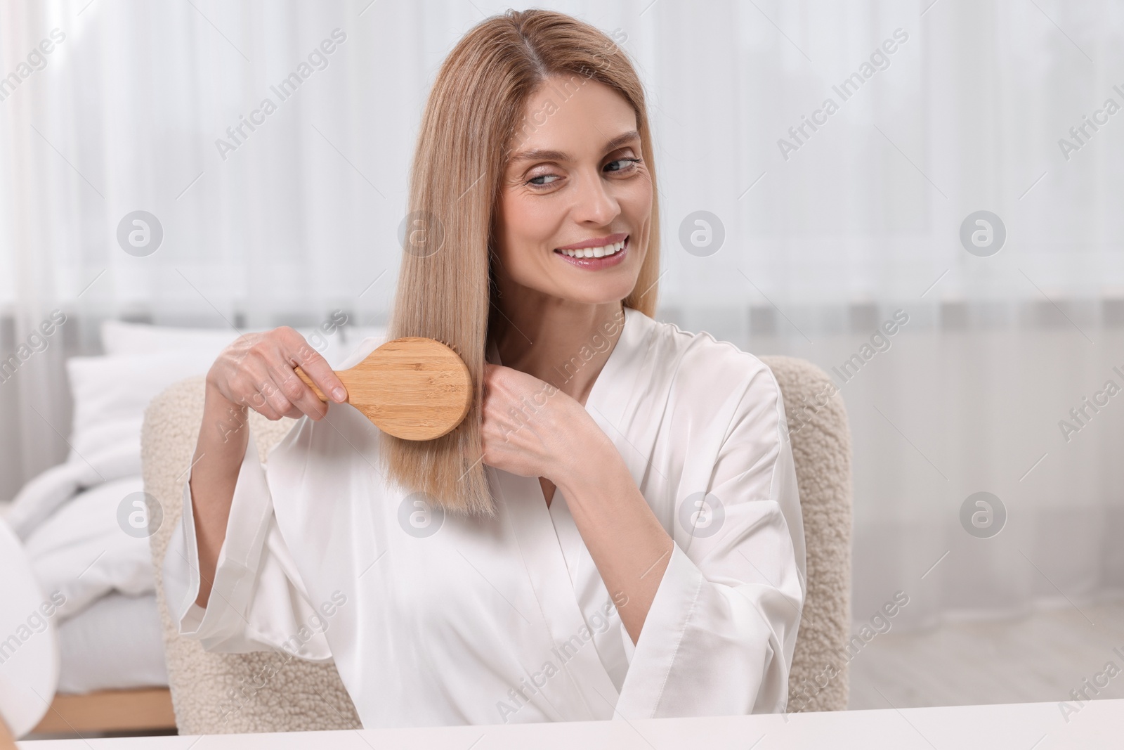 Photo of Beautiful happy woman brushing her hair in bedroom