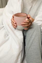 Woman with cup of coffee and soft blanket on bed, closeup