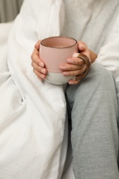 Photo of Woman with cup of coffee and soft blanket on bed, closeup