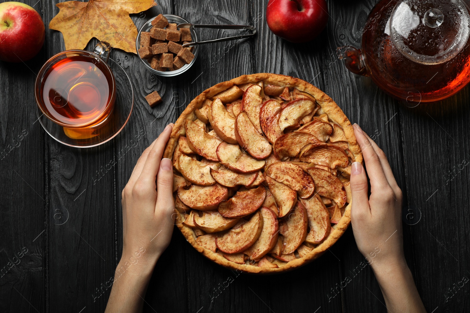 Photo of Woman with delicious apple pie at black wooden table, top view