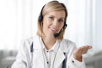 Portrait of smiling doctor in headphones having online consultation indoors