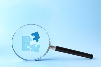 Jigsaw puzzle pieces on light blue background, view through magnifying glass