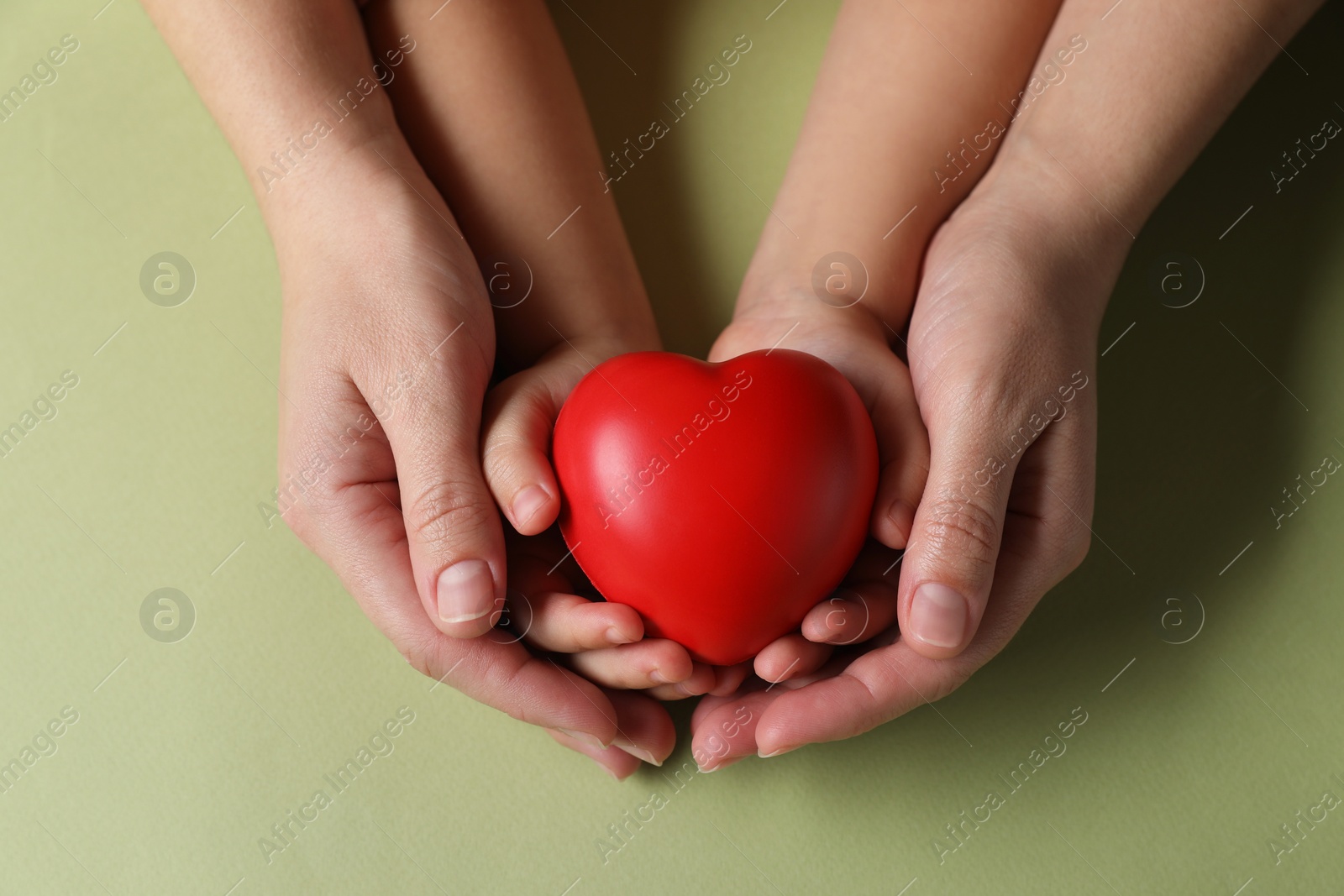 Photo of Mother and her child holding red decorative heart on light green background, top view