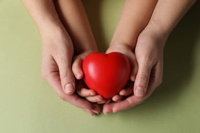 Photo of Mother and her child holding red decorative heart on light green background, top view