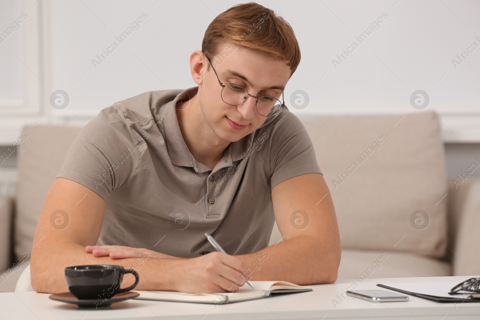 Photo of Young man writing in notebook at table indoors