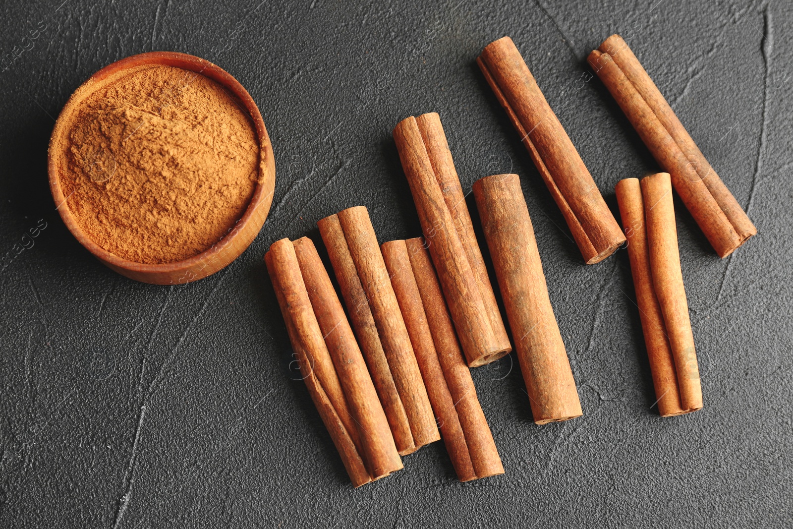Photo of Aromatic cinnamon sticks and powder on dark grey background