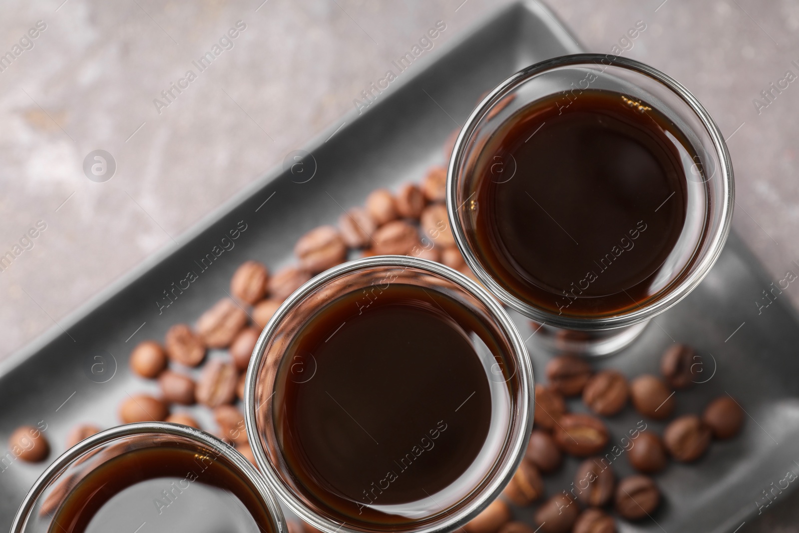 Photo of Shot glasses with coffee liqueur and beans on light grey table, top view