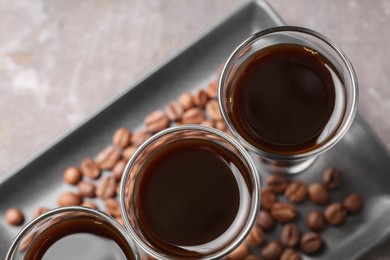 Shot glasses with coffee liqueur and beans on light grey table, top view