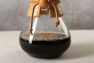 Glass chemex coffeemaker with tasty drip coffee on white table, closeup