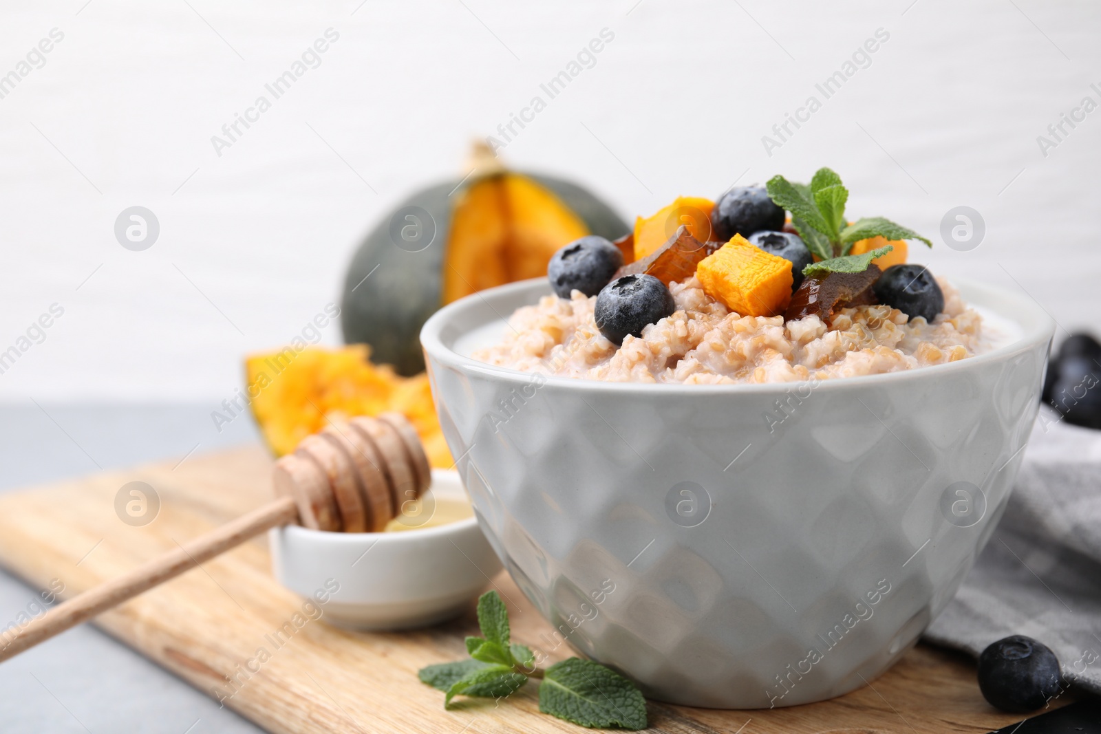 Photo of Tasty wheat porridge with pumpkin, dates and blueberries in bowl on table, closeup